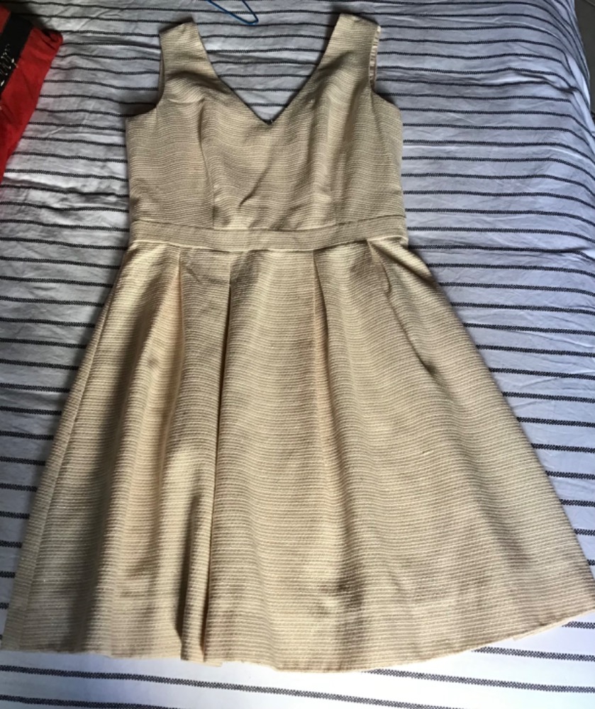 Vend robe courte sans manches, de couleur dorée/crème 
Sa coupe patineuse est très flatteuse : elle est cintrée à la taille grâce à une large bande ceinturée, puis s'évase avec d'élégants p...